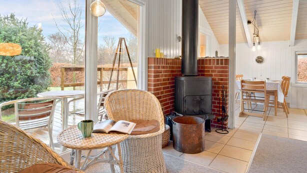 A cozy room with wicker furniture, a large window, a brick wall, and a wood-burning stove.