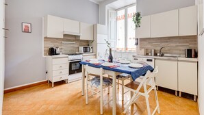 Uma cozinha moderna com armários brancos, toalha de mesa azul e uma área de refeições com cadeiras.