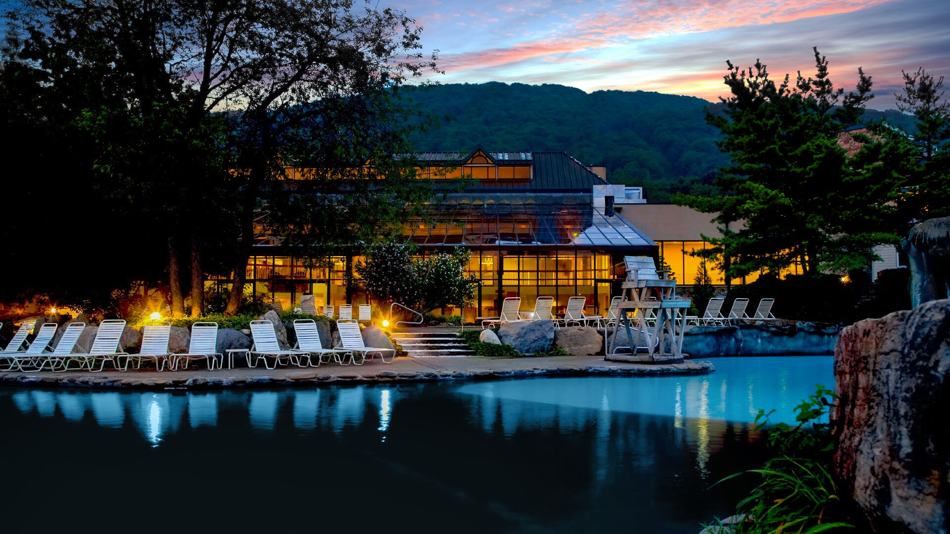 A resort with a pool, lounge chairs, and a building with large windows.