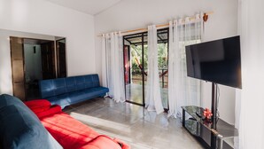 A modern living room with a blue sofa, red cushions, a glass coffee table, and a flat-screen TV. - Mini Oasis in Avellanas beach, natural pool, parking, A/C, kitchen #4 (Santa Cruz)