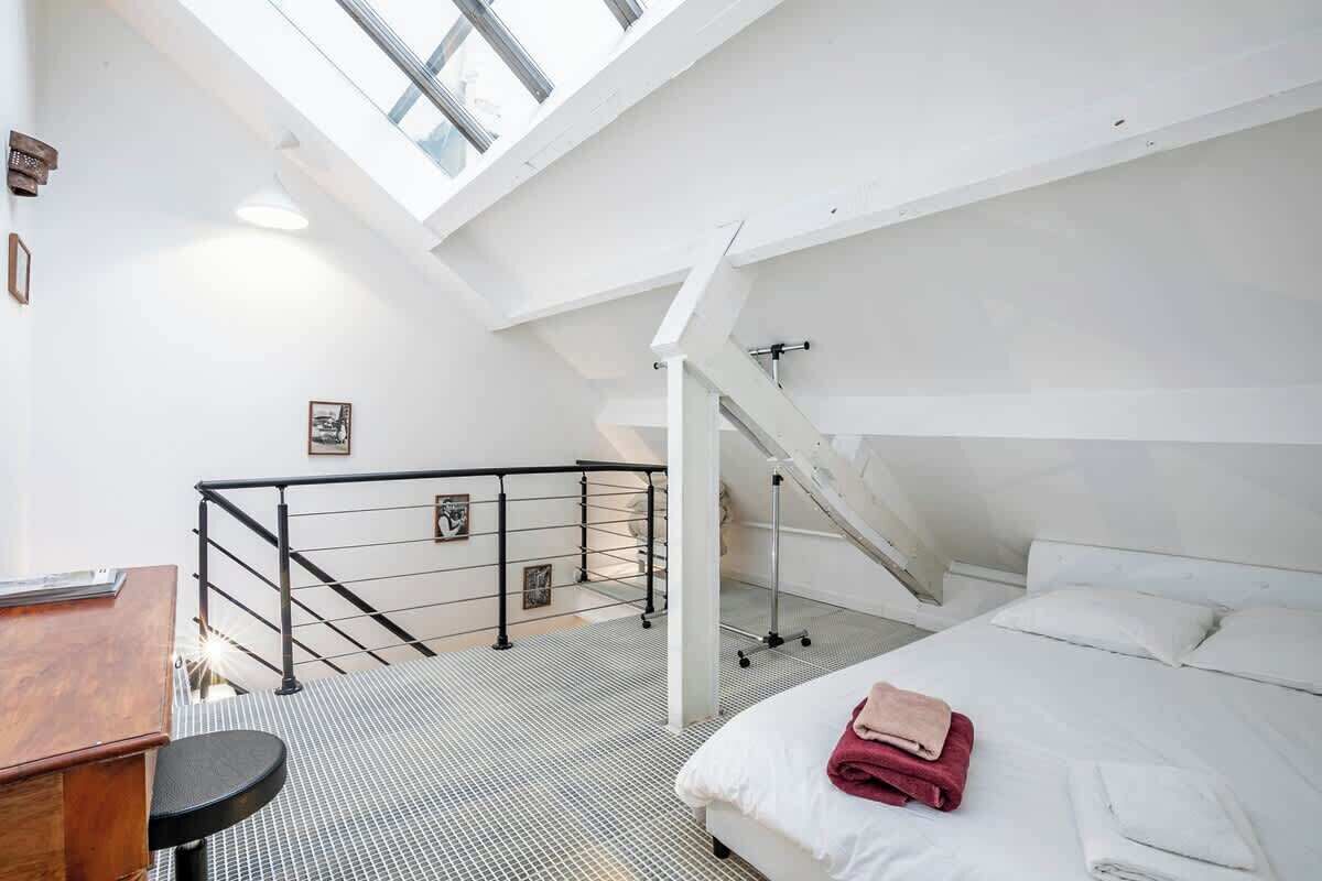 Een slaapkamer met een bed, een bureau en een trap naar een hoger gelegen verdieping.