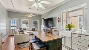 A modern kitchen with a wooden island, a dining area with a sofa and chairs, and a ceiling fan.