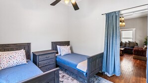A bedroom with two single beds, a ceiling fan, and a view into the living area.