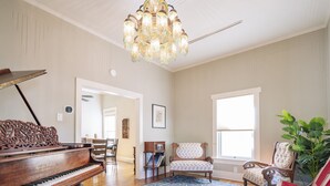 A spacious living room with a grand piano, a chandelier, and a large window.