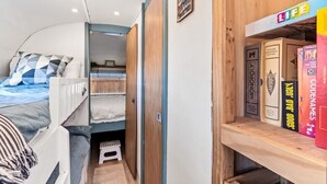 A compact room with bunk beds, a small window, and a bookshelf with books. - NEW! Cozy, Desert Dream Airstream with Firepit (Tombstone)