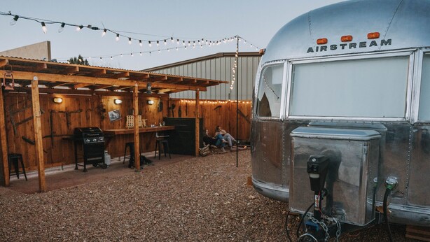Een vintage AIRSTREAM caravan met een houten pergola, lichtjes, een barbecue en een grindpad.