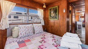 A bedroom with a bed, curtains, a painting, and a view of an RV outside. - Retro Vintage Spartan Trailer (Tombstone)