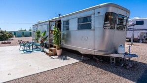 A stationary RV with a covered patio area, including outdoor furniture and potted plants. - Retro Vintage Spartan Trailer (Tombstone)