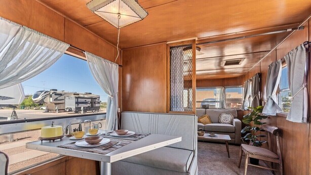 A cozy RV interior with a dining area, seating, and a view of the outside. - Retro Vintage Spartan Trailer (Tombstone)
