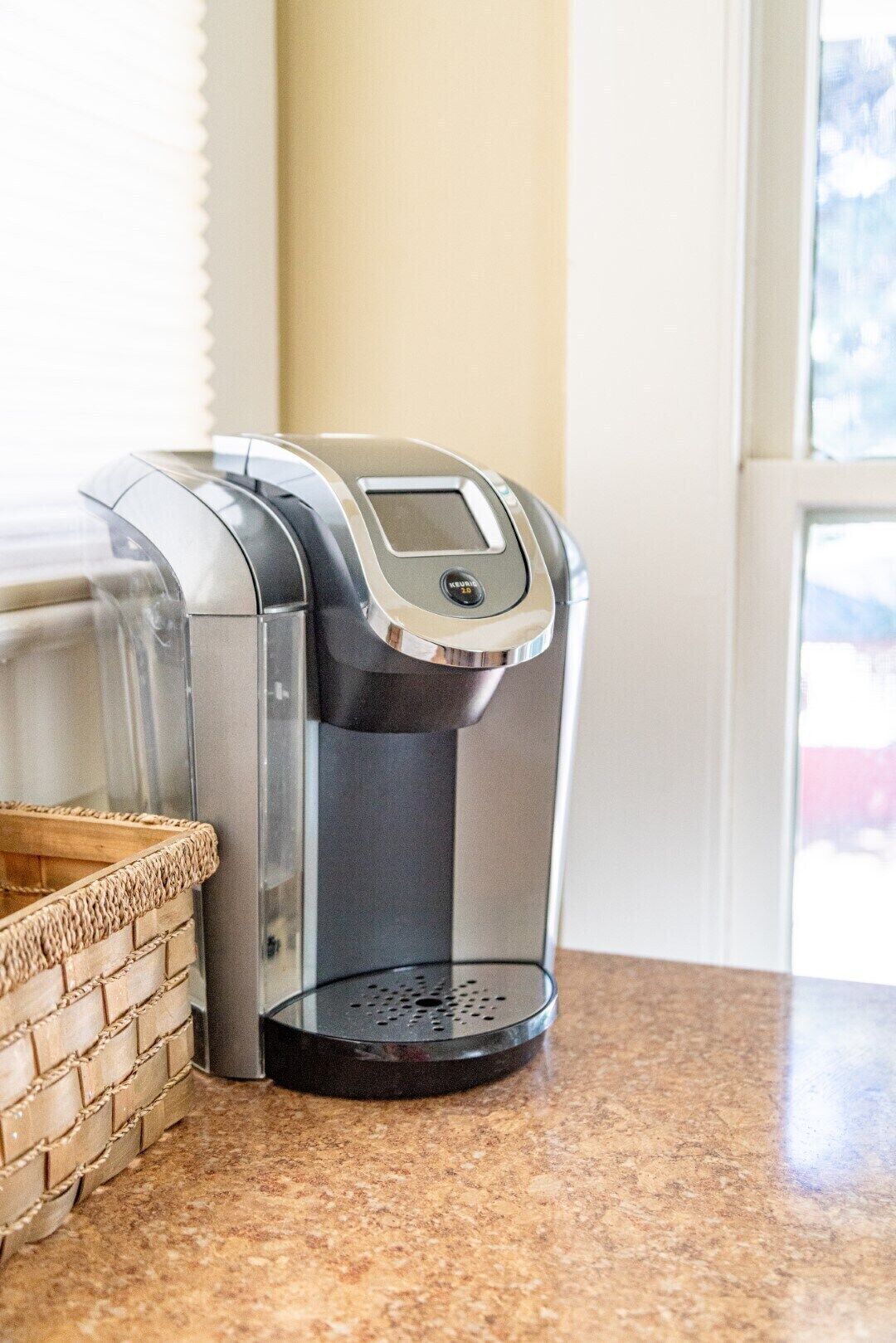 A coffee maker on a kitchen counter with a basket beside it.