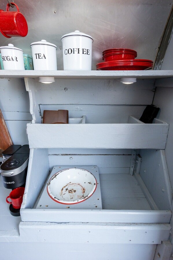 Une cuisine avec des meubles blancs, des récipients étiquetés pour le sucre, le thé et le café, et un égouttoir rouge.