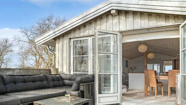 A cozy outdoor seating area with a wooden bench and a cushioned sofa, a wooden coffee table, and a glass door leading to an interior space with a dining table and chairs. - 1 bedroom awesome apartment in Grevinge (Grevinge)