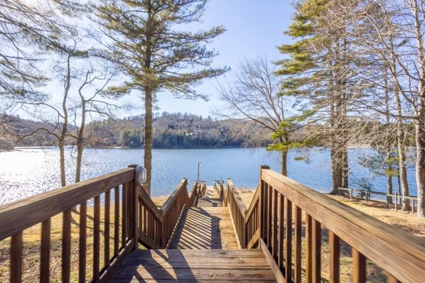 A wooden deck leading to a lake with trees on either side.