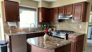 A kitchen with granite countertops, wooden cabinets, a dishwasher, a stove, and a window with blinds. - Beautiful Waukesha Home (Waukesha)