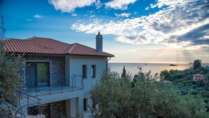 Ein Küstenhaus mit einer Stein-Fassade, einem roten Ziegeldach und einem Balkon mit Blick auf das Meer.