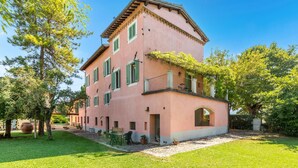 A pink villa with a balcony, a garden, and a paved driveway. - Cozy home in Spoleto with WiFi (Spoleto)