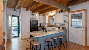 A kitchen with a central island, bar stools, wooden beams, and white cabinetry.