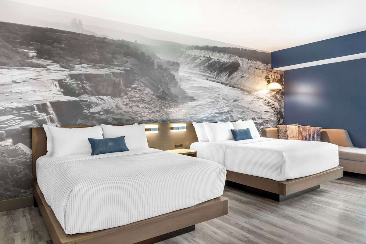 Ein Hotelzimmer mit zwei Betten, einem großen Wandgemälde einer felsigen Landschaft und einer blauen Akzentwand.