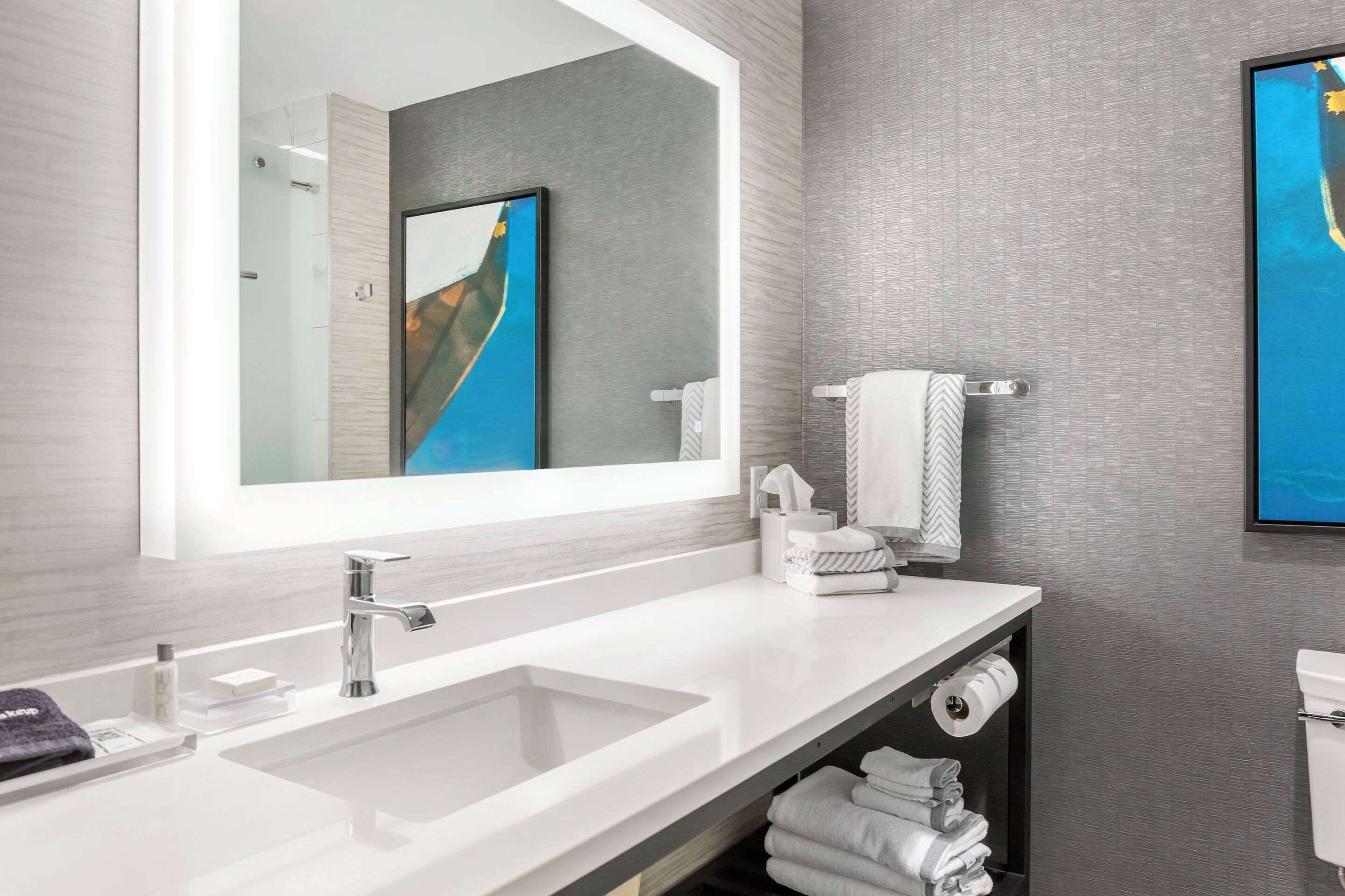 Un baño moderno con un espejo grande, un lavamanos blanco y un perchero para toallas.
