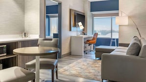 Une chambre d’hôtel moderne dotée d’un coin repas, d’un canapé, d’un bureau et d’une grande fenêtre donnant sur un paysage agréable.