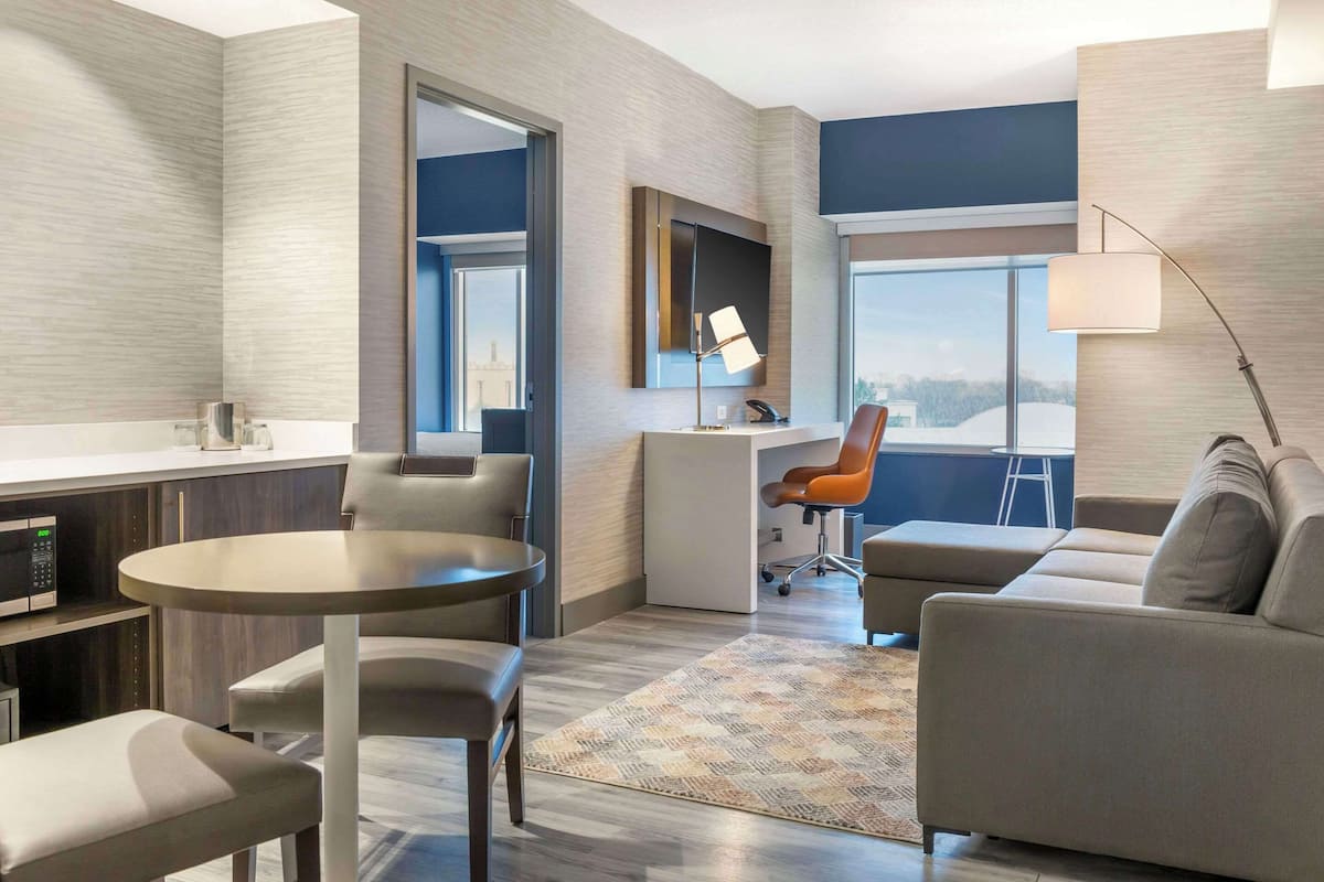 Ein modernes Hotelzimmer mit Essbereich, einer Sitzecke, einem Schreibtisch und einem großen Fenster mit Blick.