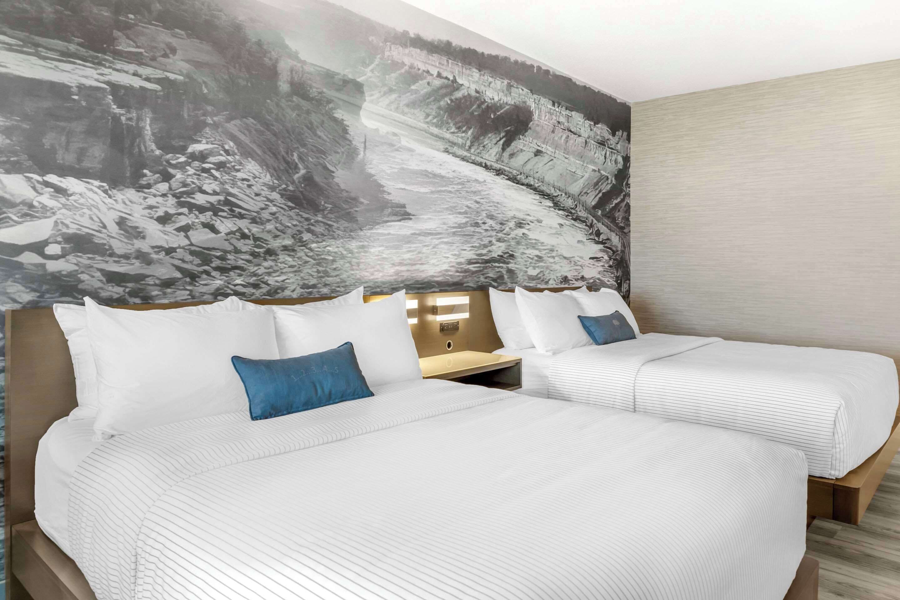 A hotel room with two beds, a large mural on the wall, and a wooden headboard.