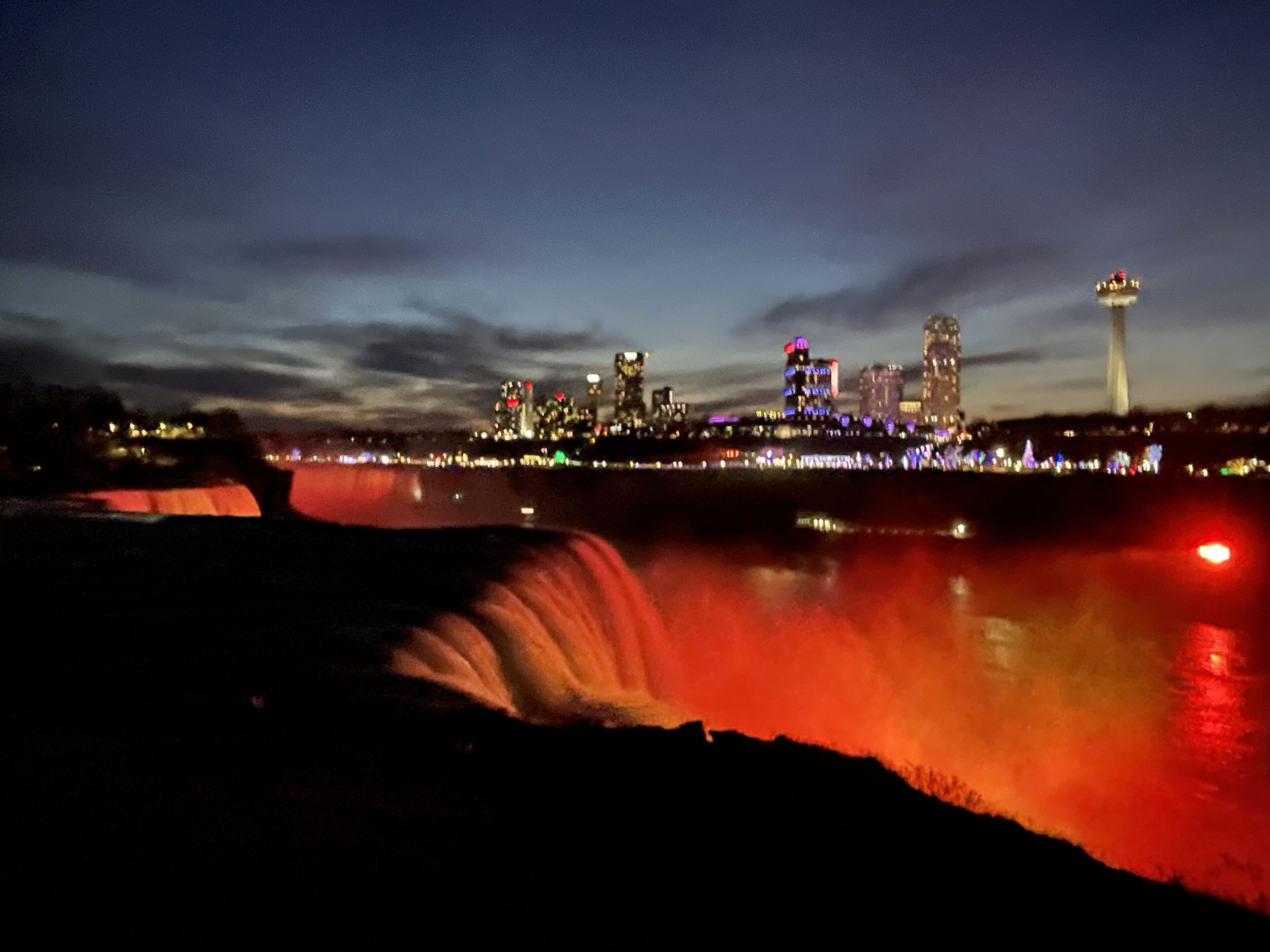 A nighttime cityscape with illuminated buildings and a waterfall.