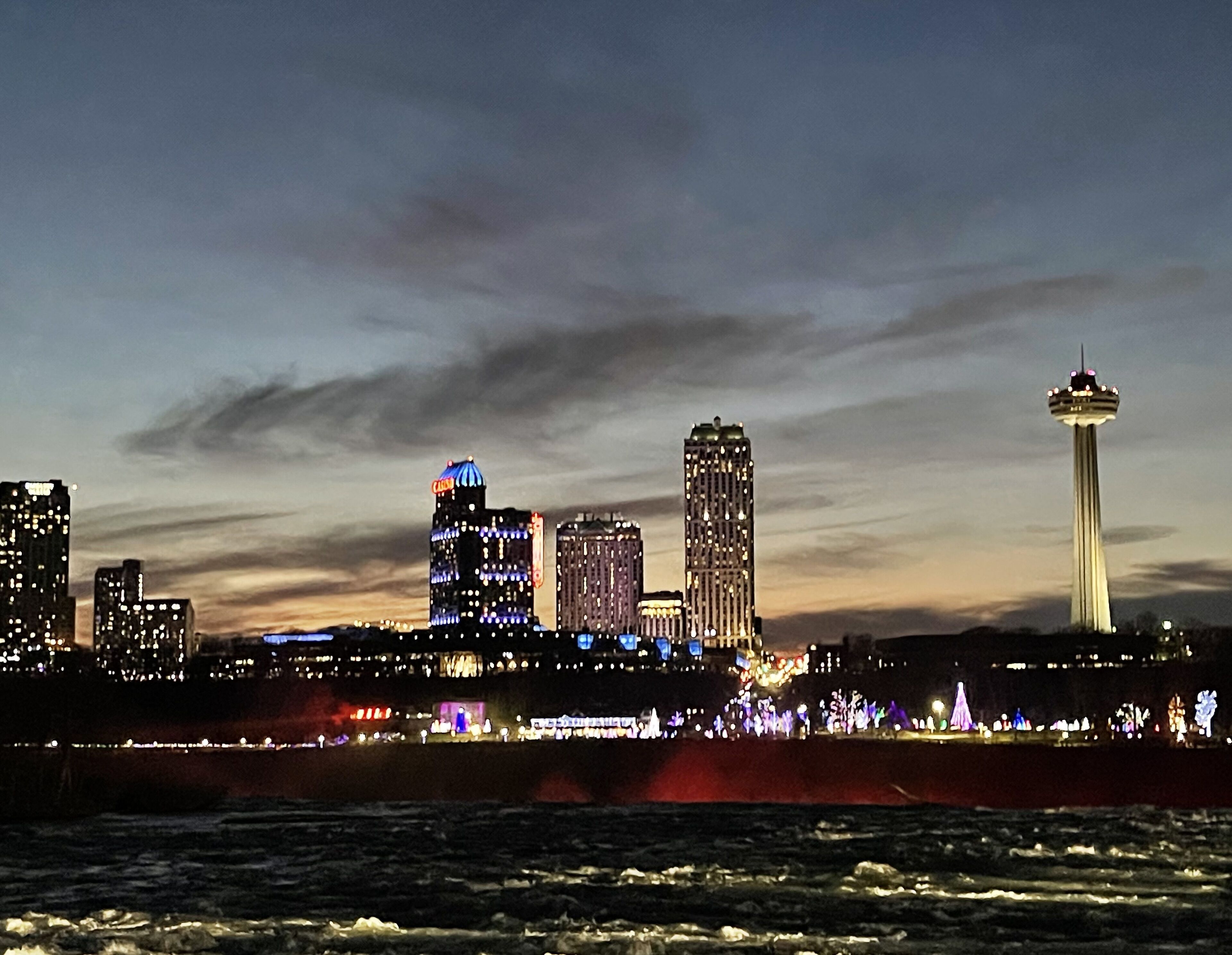 A nighttime cityscape with illuminated buildings and a prominent tower.