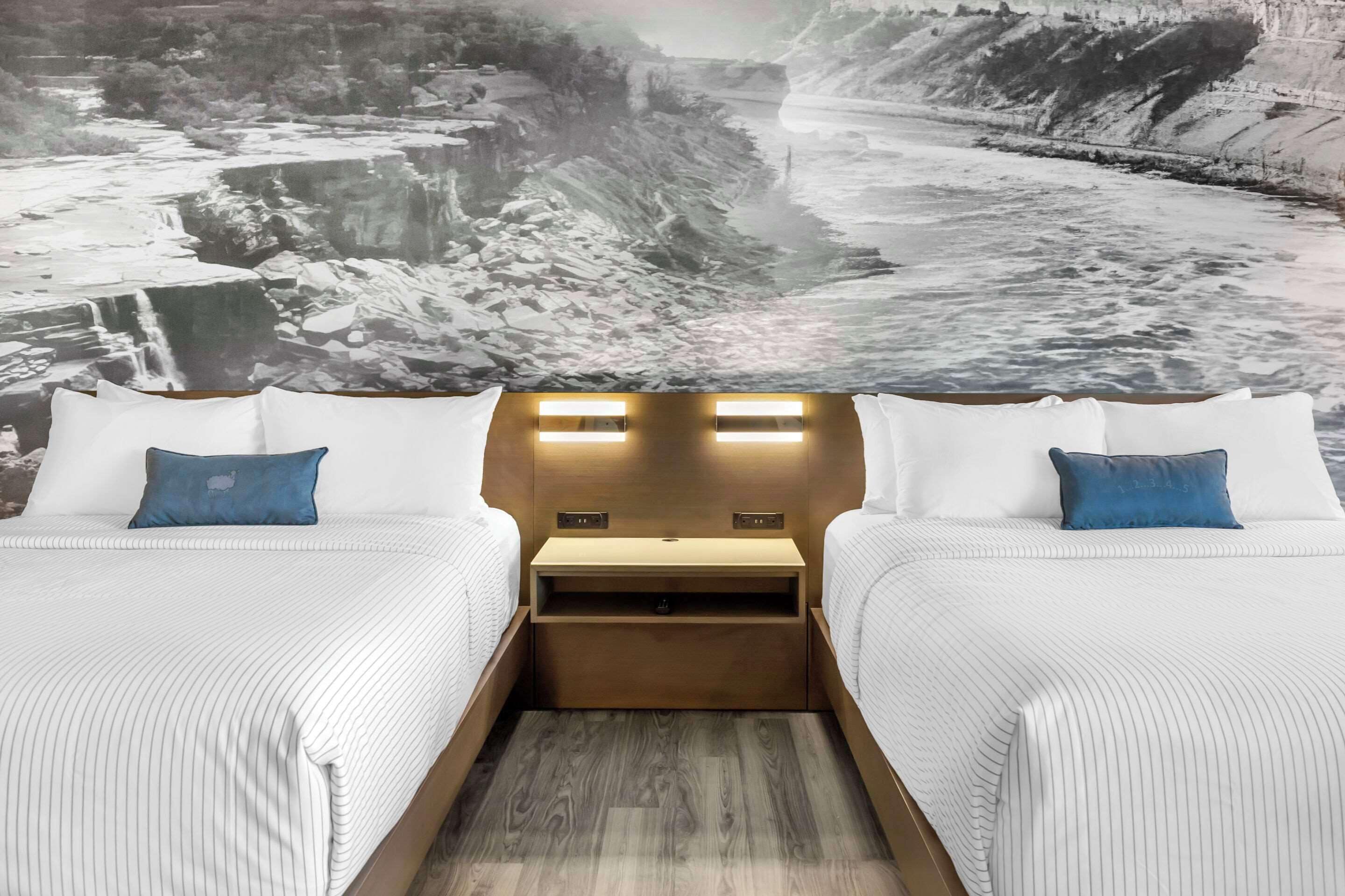 Een tweepersoonskamer met twee bedden, een nachtkastje ertussen en een muurschildering van een rivierlandschap.