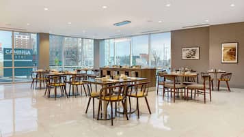 Eine moderne Hotelhalle mit mehreren Gastronomiebereichen, großen Fenstern mit Blick auf die Stadt und einem sauberen, glänzenden Boden.