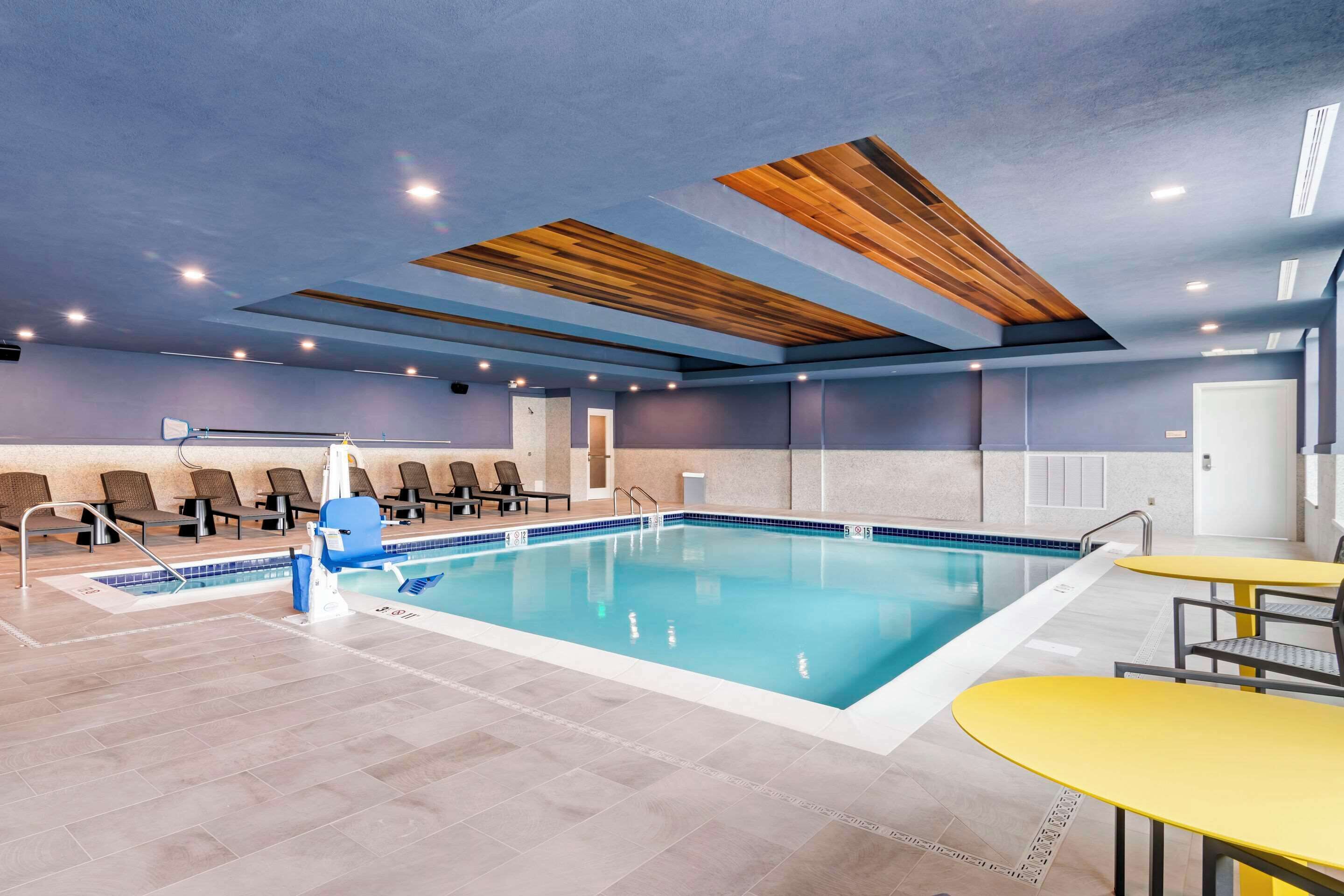 Una piscina interior moderna con techo de madera, suelo de baldosas y zonas de estar.