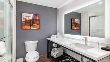 Un baño moderno con un lavabo blanco, un espejo grande y un inodoro. Hay toallas y artículos de aseo en la encimera.