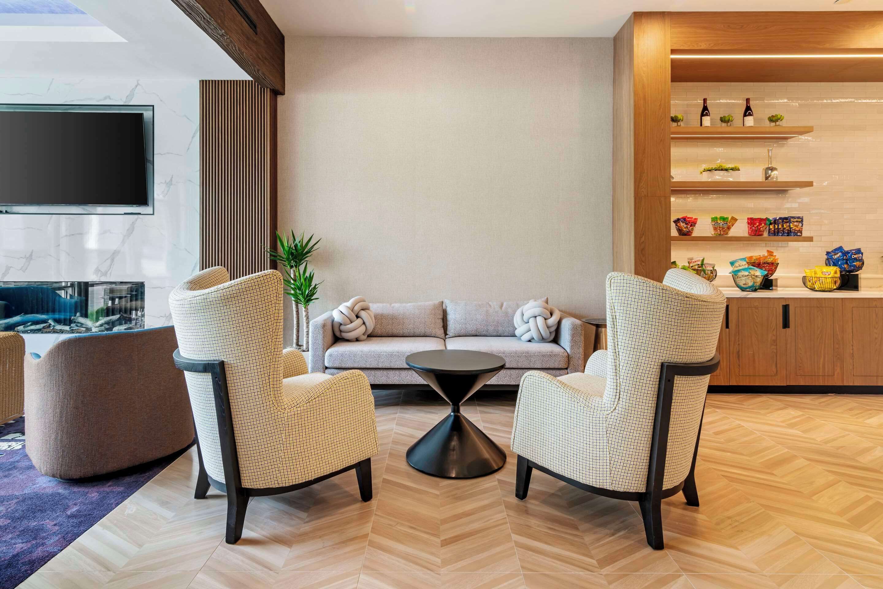 Una sala de estar moderna con un sofá, dos sillones, una mesa de centro y un televisor montado en una pared de mármol.