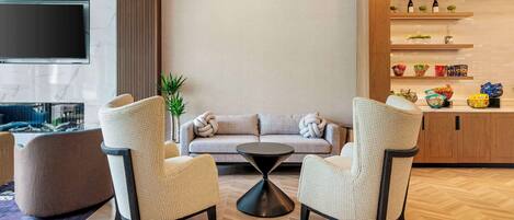 Un salon moderne comprenant un canapé, deux fauteuils, une table basse et un téléviseur fixé au mur, qui est recouvert de marbre.