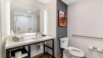 A modern bathroom with a white sink, mirror, and toilet. There is a towel rack and a shelf with toiletries.
