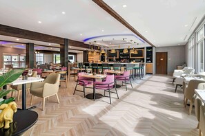 A modern restaurant with a herringbone floor pattern, wooden beams, and pendant lighting.