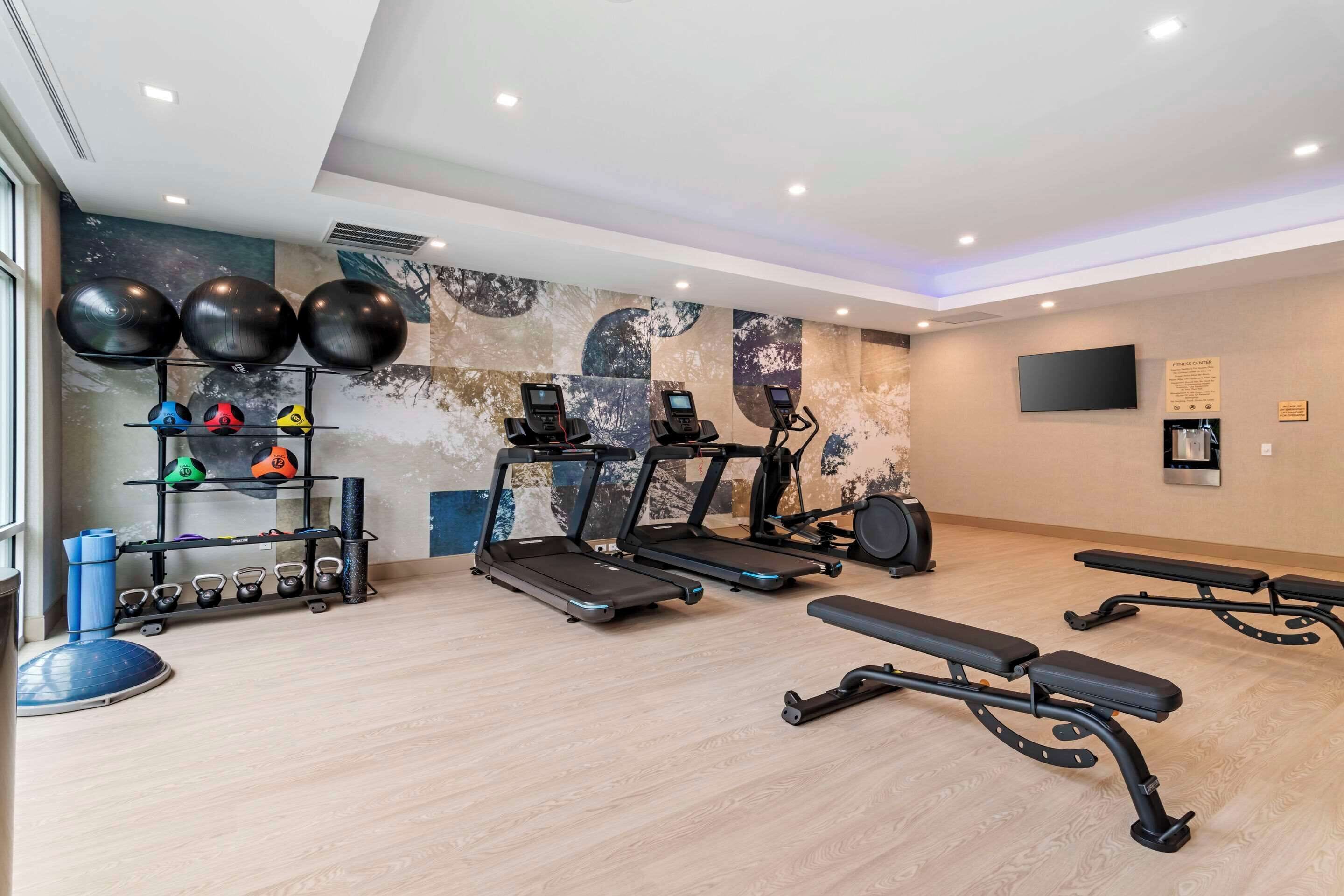 Un gimnasio con cintas de correr, bicicletas estáticas y pelotas de ejercicio.
