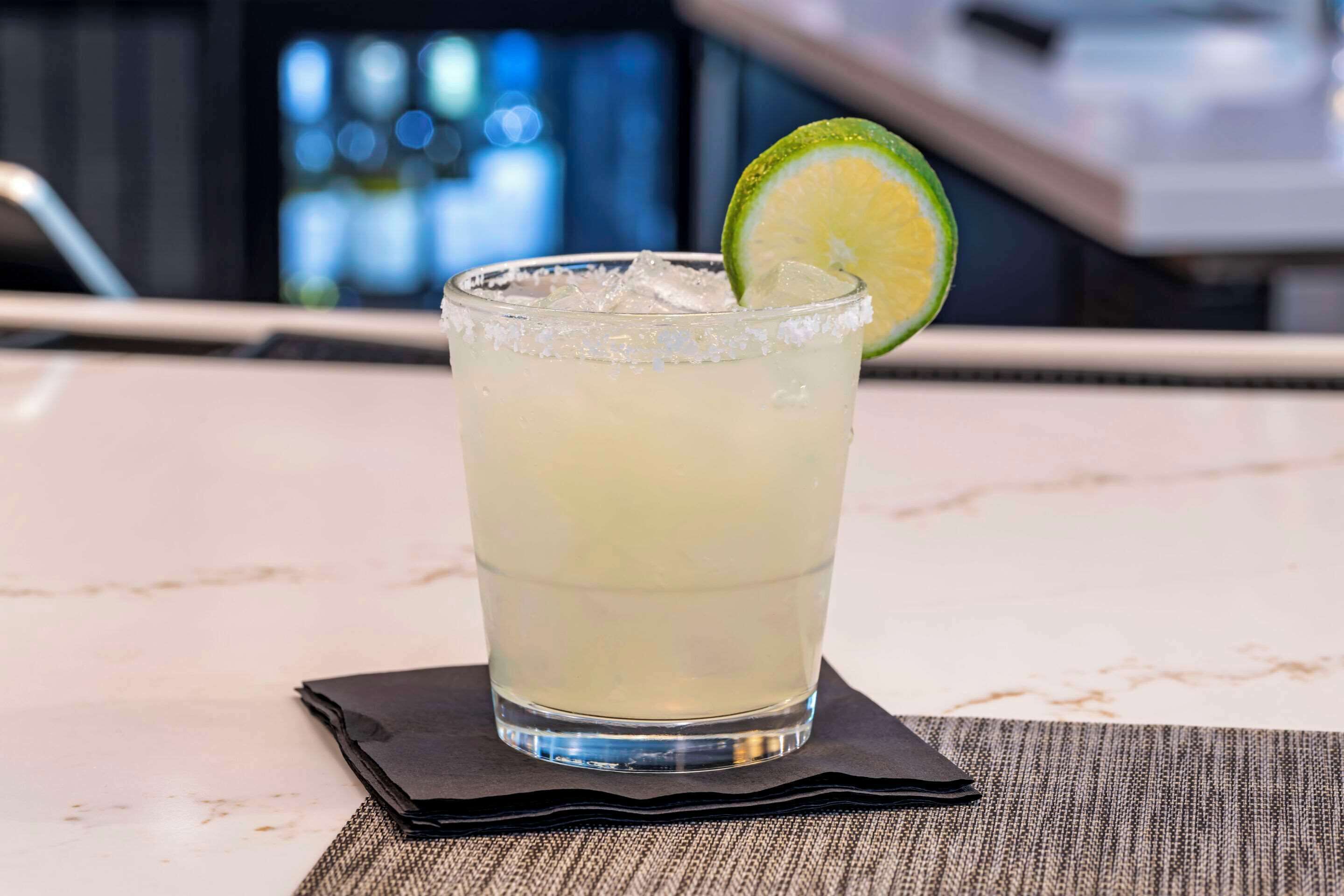 A glass of a light-colored beverage with ice cubes and a lime slice on a coaster.