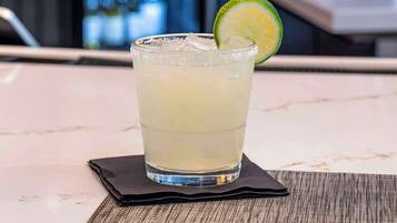 A glass of a light-colored beverage with ice cubes and a lime slice on a coaster.