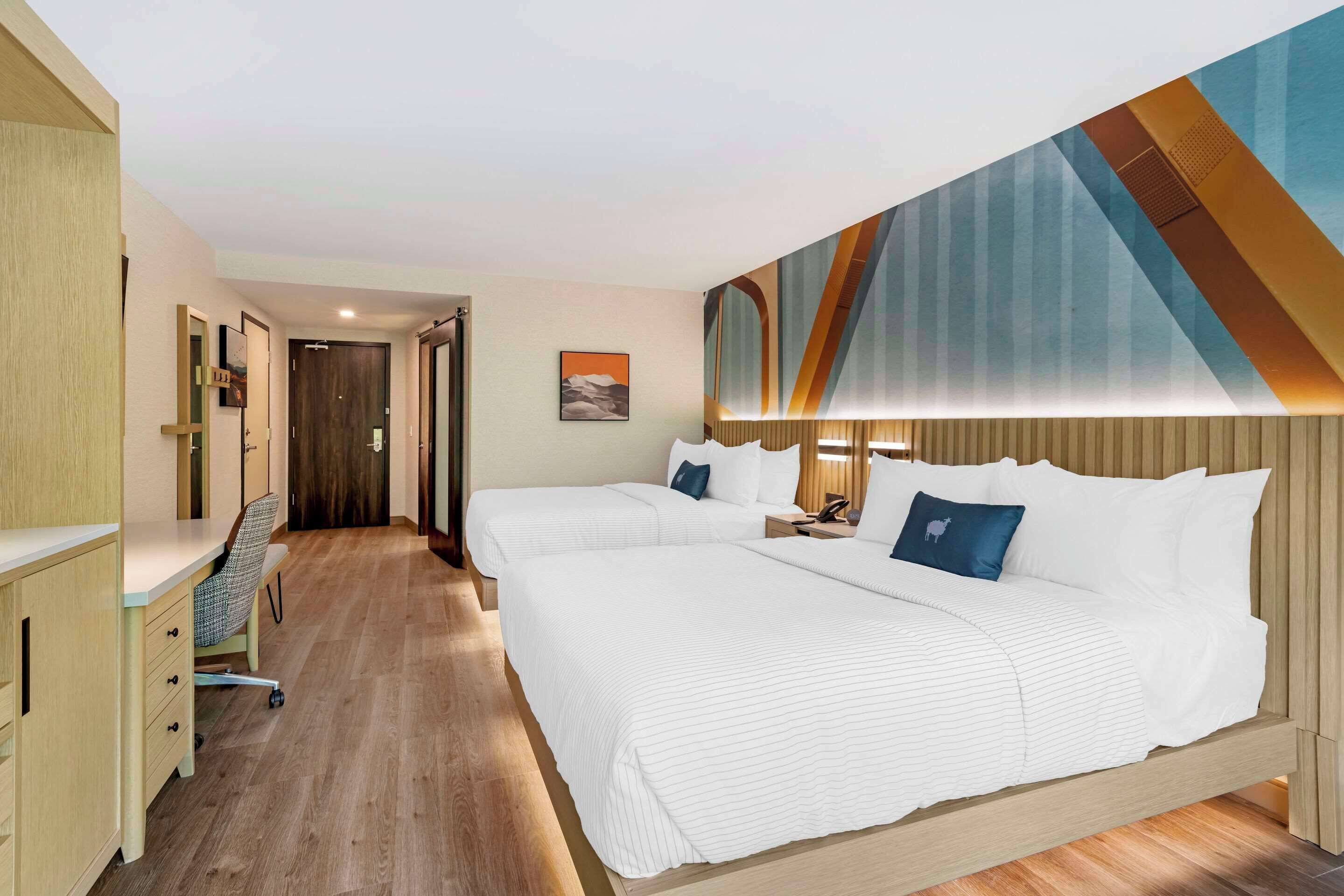 A hotel room with two beds, a desk, and a chair.
