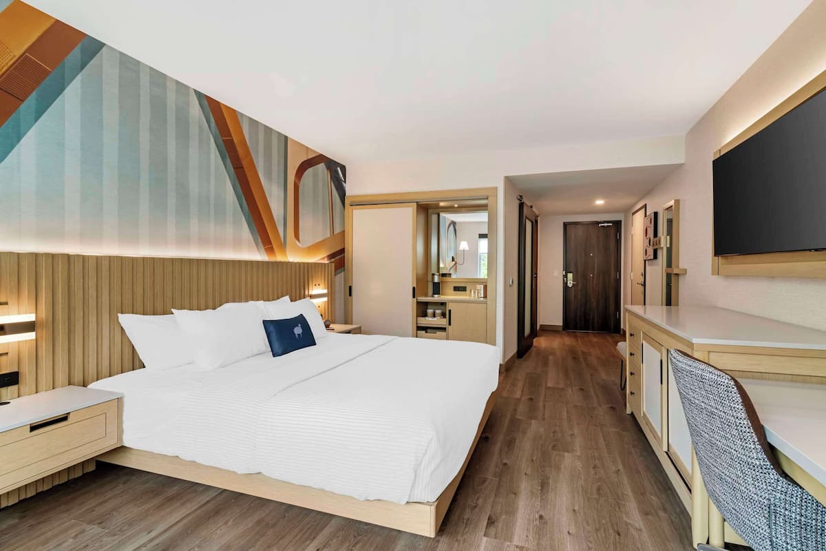 Moderni hotellihuone, jossa on suuri sänky, yöpöydät, työpöytä ja suuri peili.