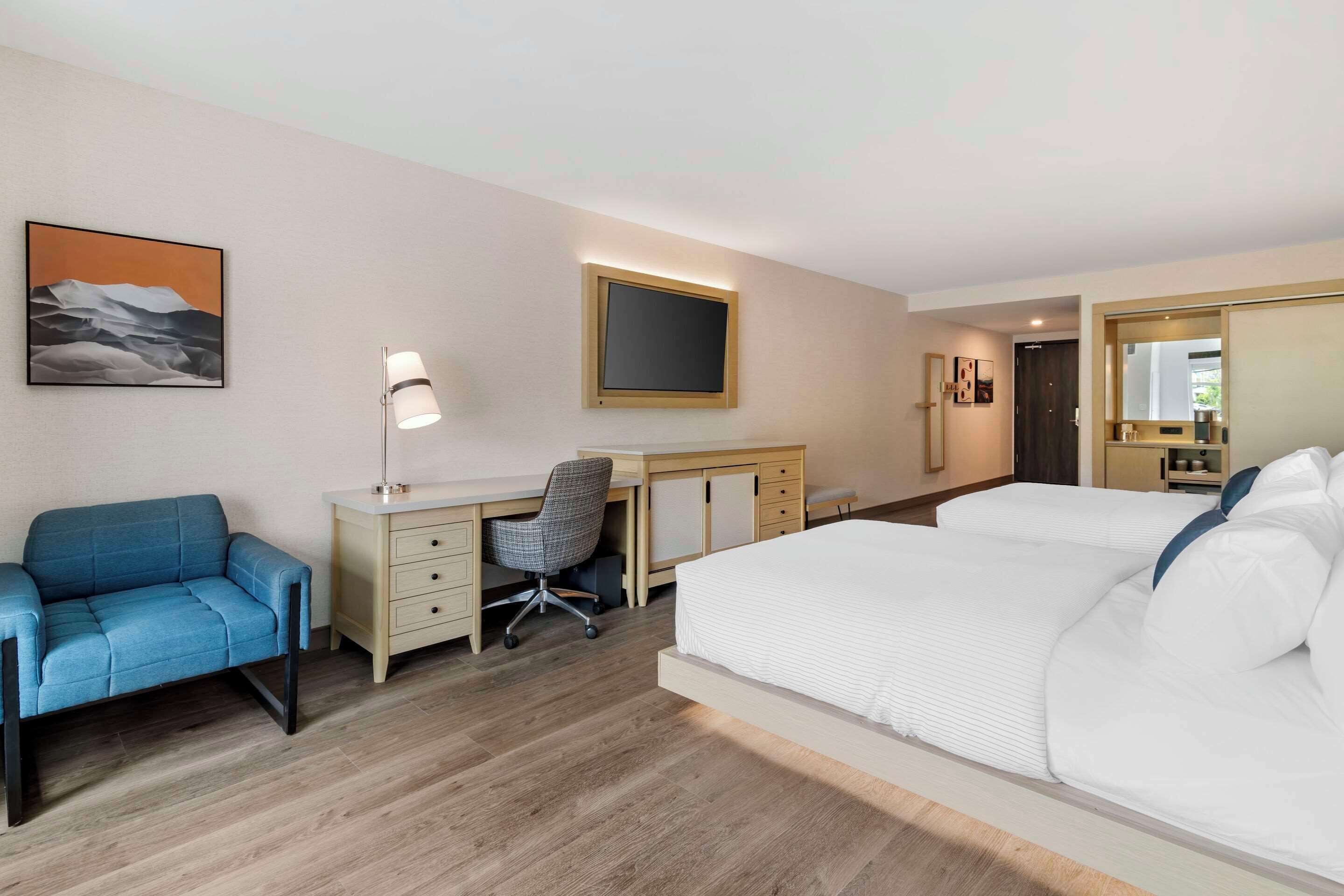 Una habitación de hotel con una cama, un escritorio con silla, un sofá, una lámpara de escritorio y un cuadro en la pared.