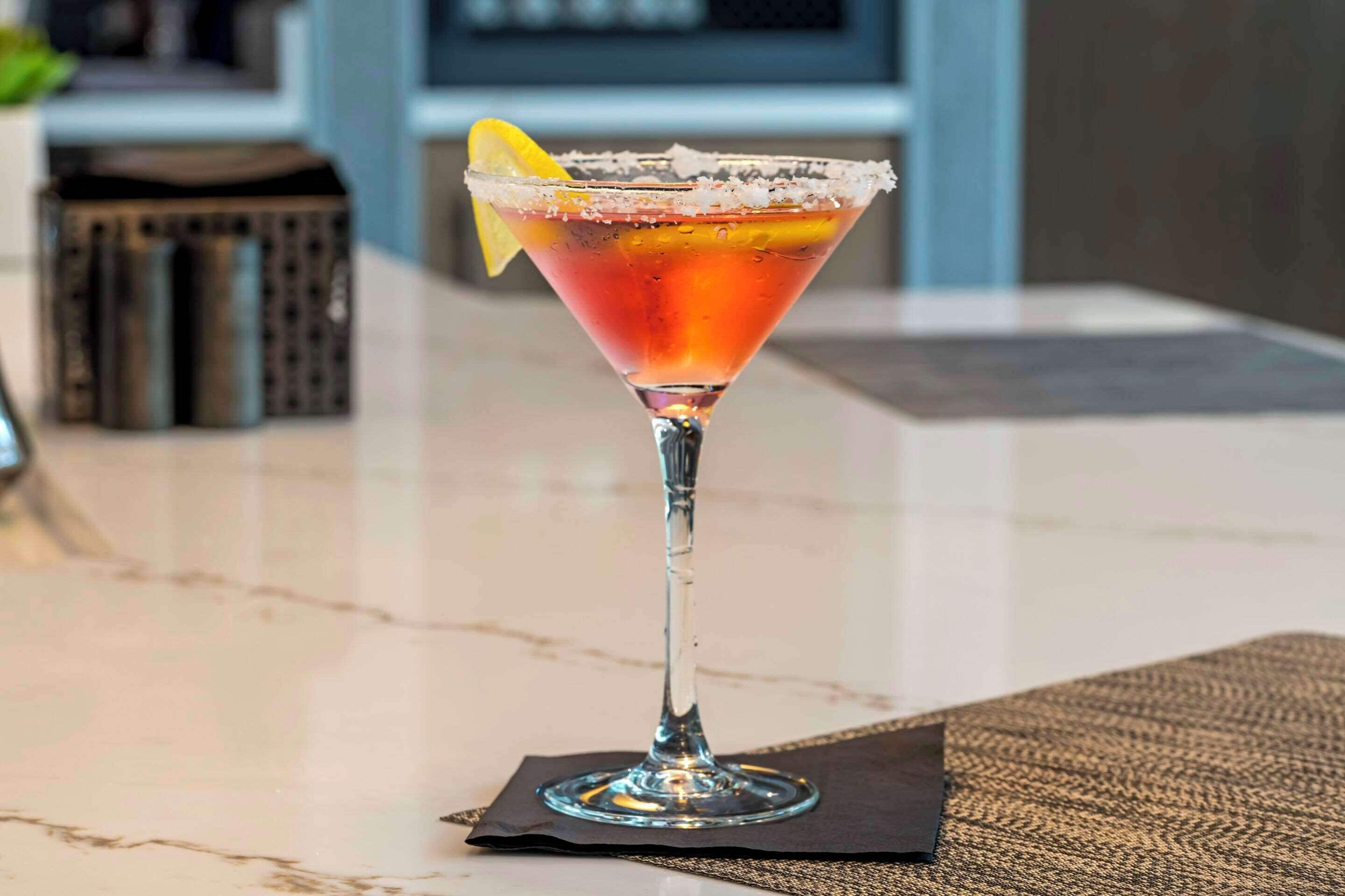 Ein Cocktail im Martiniglas mit gesalzenem Rand, garniert mit einer Zitronenscheibe, auf einem Marmortisch.