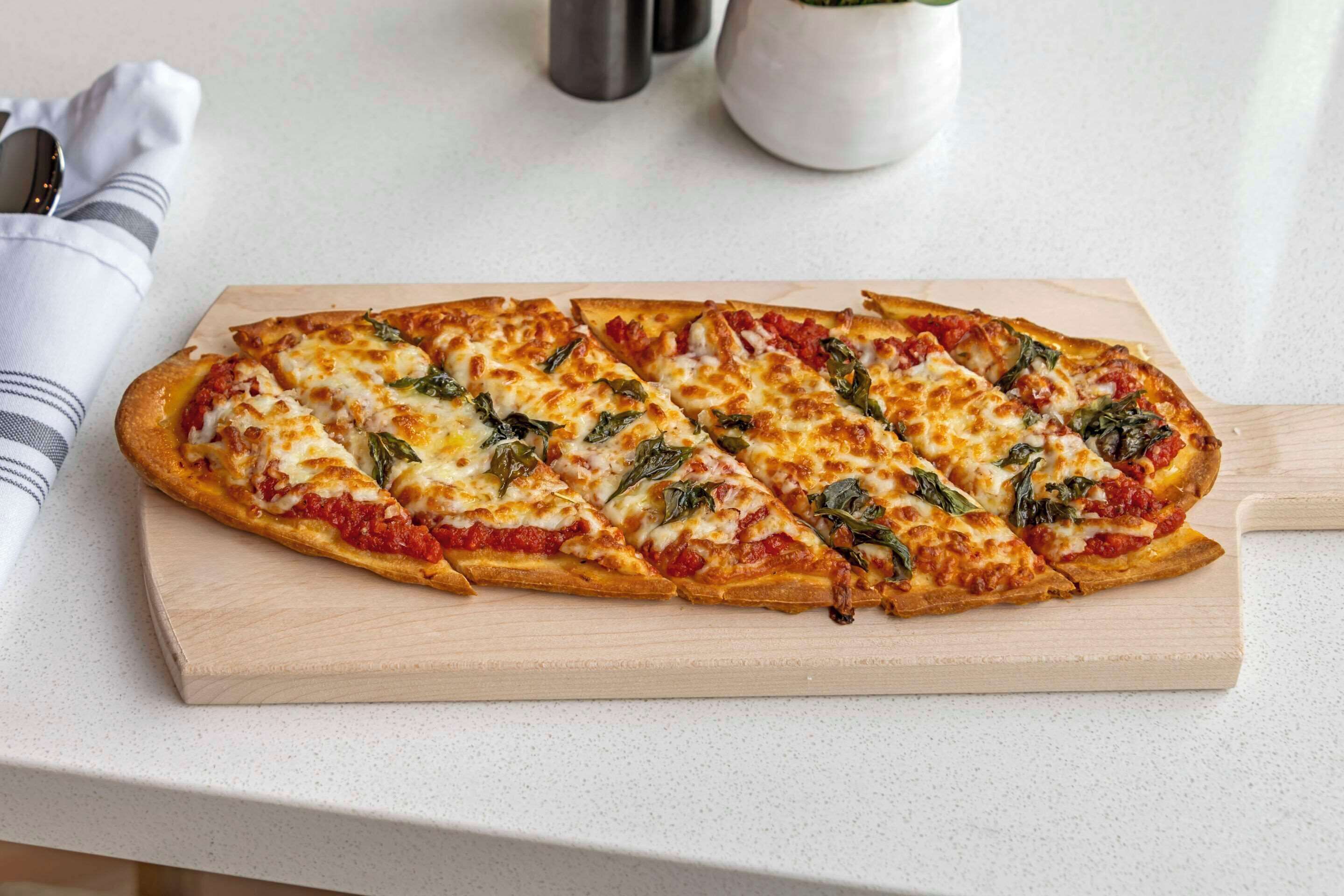 Une pizza servie sur une planche en bois.