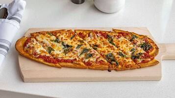 Une pizza servie sur une planche en bois.