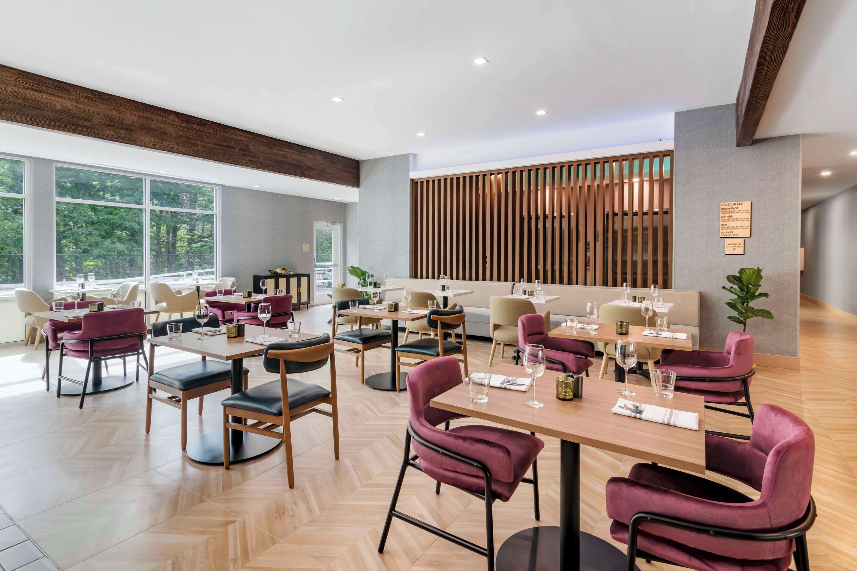Um restaurante moderno com piso de madeira, mesas com tampos de mármore e cadeiras vermelhas acolchoadas.