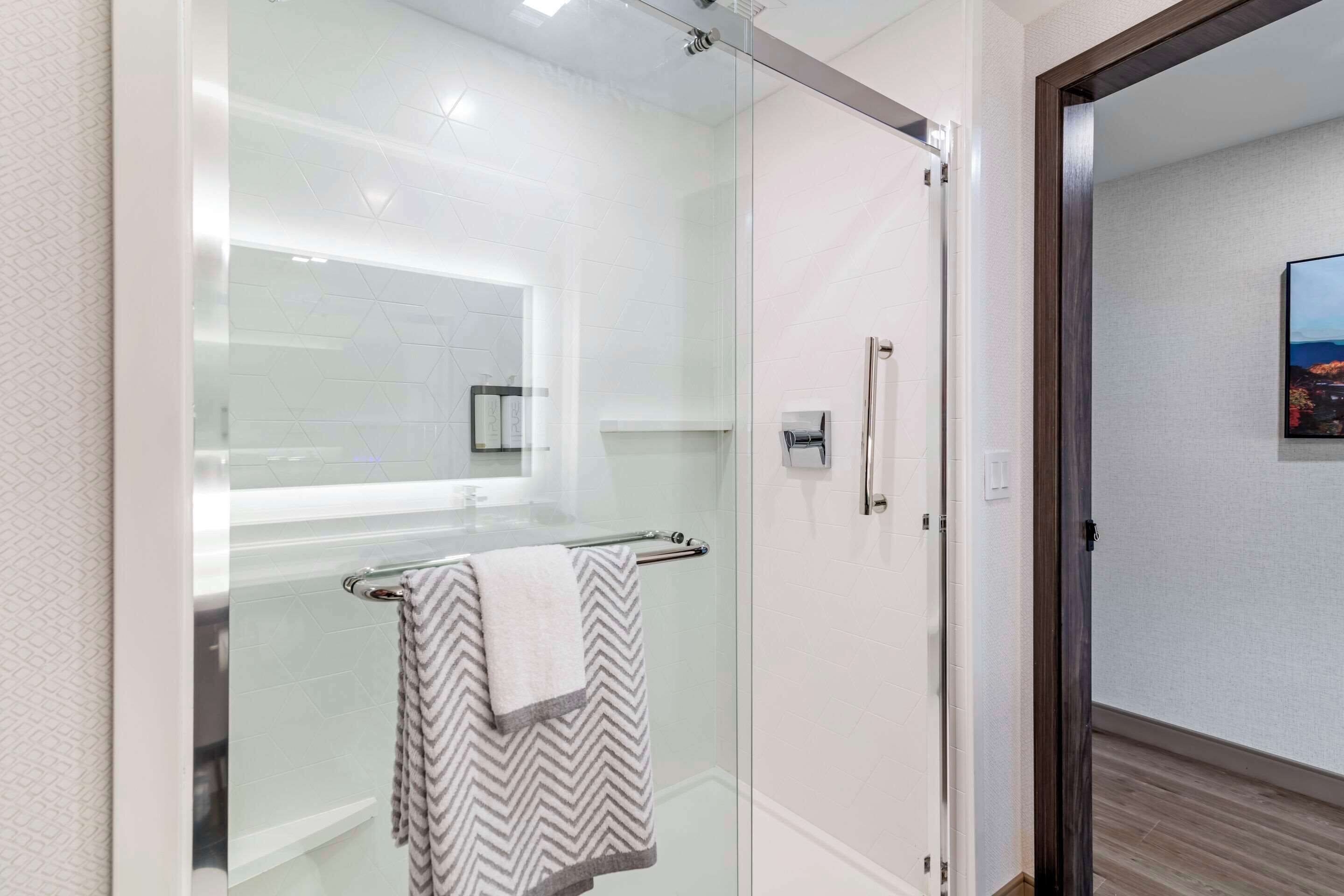 A modern bathroom with a glass shower enclosure, a towel rack with a striped towel, and a visible door leading to another room.