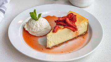 Ein Stück Käsekuchen mit Erdbeeren und eine Kugel Vanilleeis auf einem Teller.