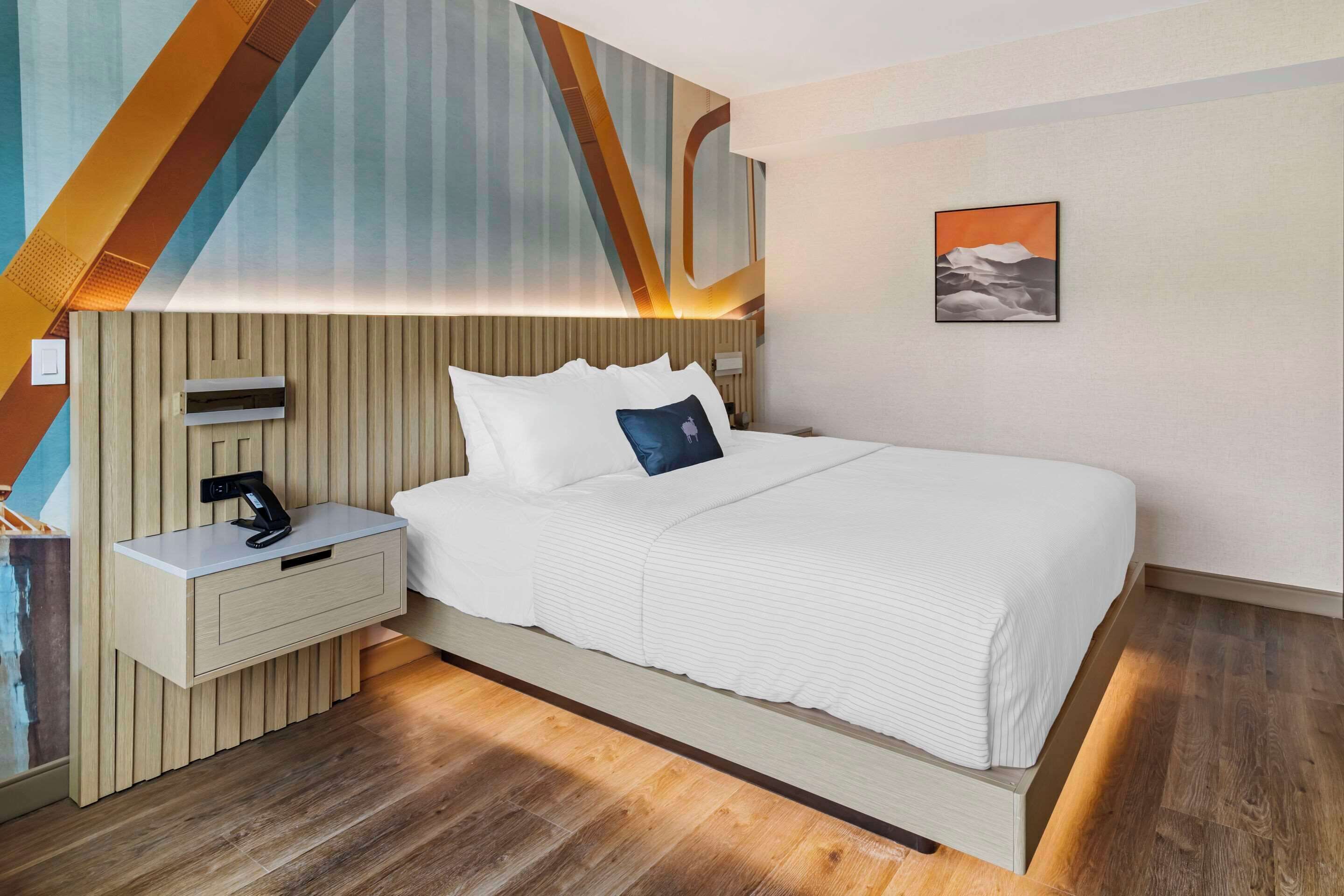Ett modernt hotellrum med en stor säng, ett nattduksbord med en telefon och en väggmonterad lampa.
