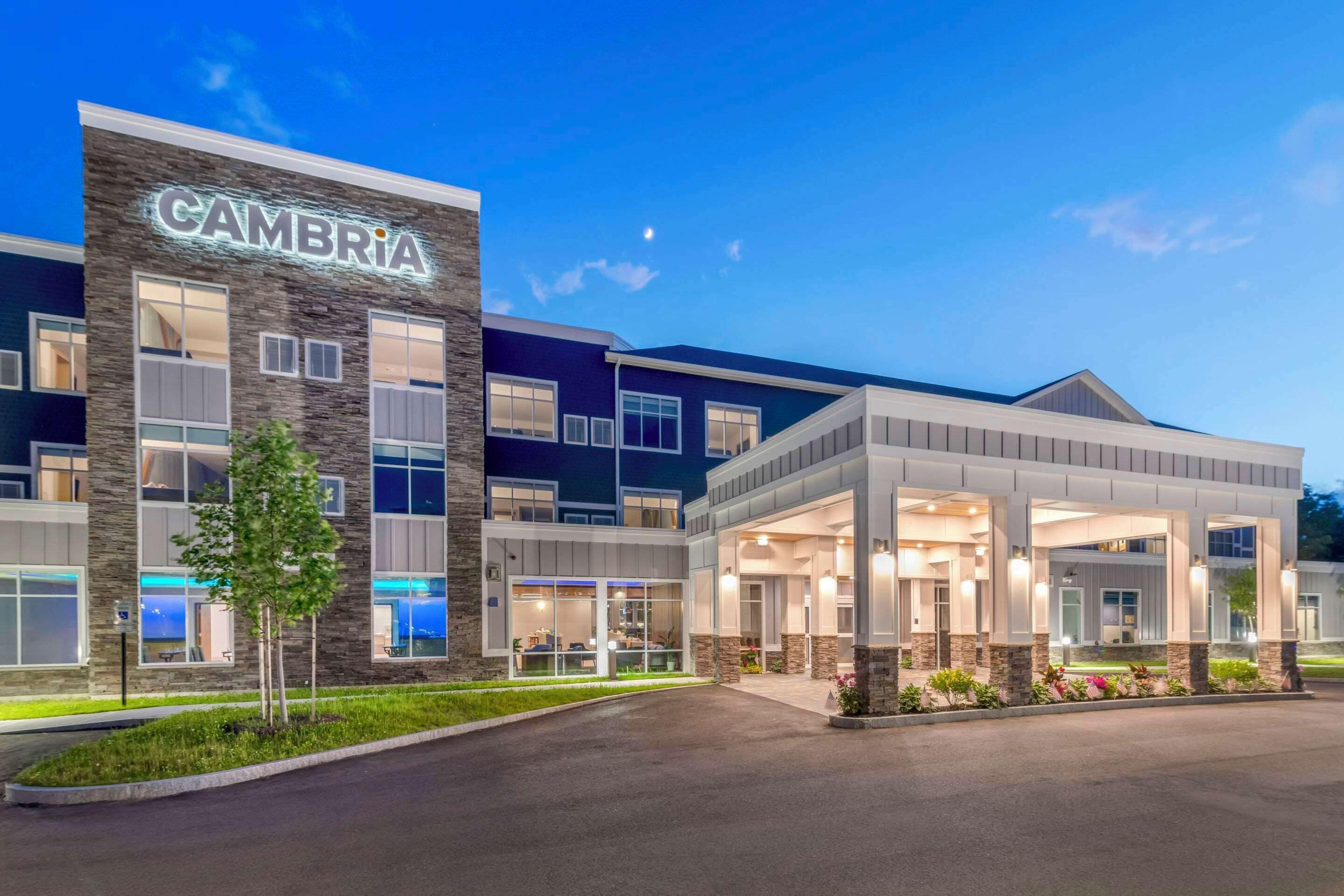 Un bâtiment moderne orné d’une enseigne « CAMBRIA », doté d’une entrée abritée et d’un espace paysager agrémenté d’arbres.